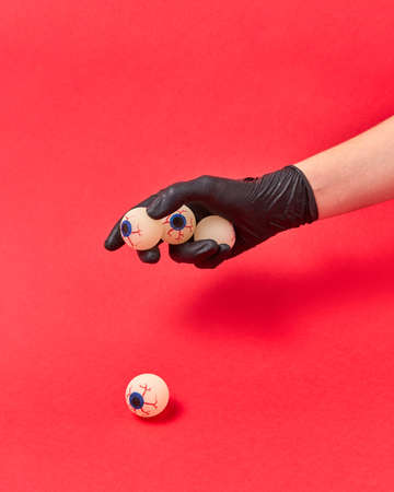Woman hand in a black glove holds human eyeballs on a red background, copy space. Halloween simbol.の写真素材