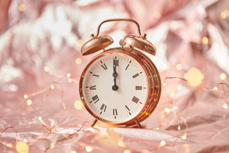Golden alarmclock with time is midnight on a shiny golden abstract background with string of lights. Greeting card.の写真素材