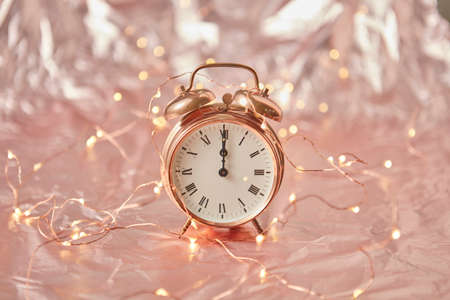 Golden alarm clock with time is midnight on a shiny cooper abstract background with string of lights, copy space. Greeting card.の写真素材