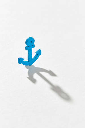 Long hard shadows on a ligth grey background from small blue plastic anchor toy with copy space.の写真素材