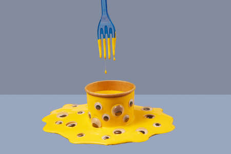 Plastic fork and drops of yellow paint above can in puddle with googly eyes.の写真素材