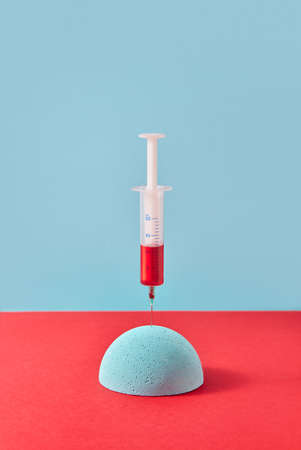 Injection of syringe with red liquid into foam hemisphere.の写真素材