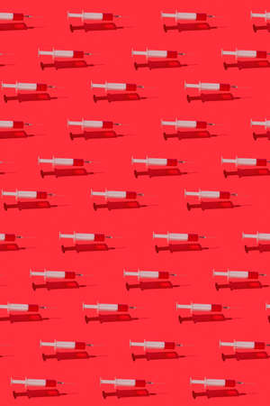 Healthcare medicinal pattern from floating surgical disposable syringes with red liquid or blood above red background with hard shadows and reflections.の写真素材
