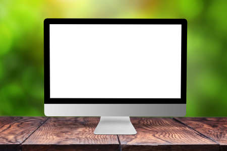 Blank white mock up computer monitor on a wooden table against blurred green natural background with bokeh, copy space. Working outside office concept.の写真素材