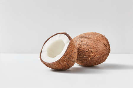 Whole natural exotic ripe coconut fruit with half on a duotone light grey background with soft shadows, copy space. Vegetarian concept.の写真素材