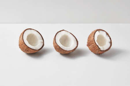 Fruits pattern from three exotic organic natural halves of ripe coconuts on a duotone light grey background with soft shadows, copy space. Vegetarian concept.の写真素材