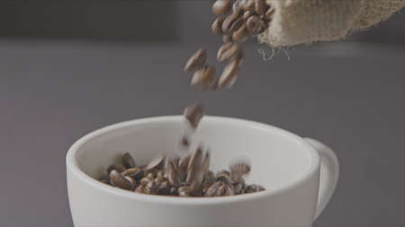 Roasted coffee beans poured from the bag, in a cup around a dark background.の写真素材