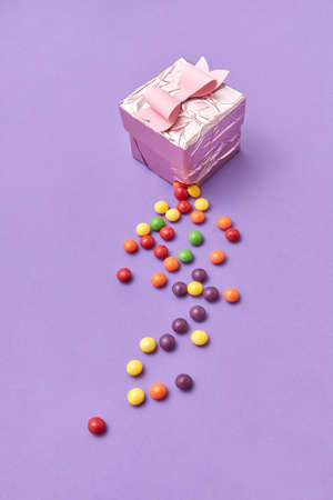 Greeting card from decorative present box ripped and with multicolored candy on a purple background copy space.の写真素材