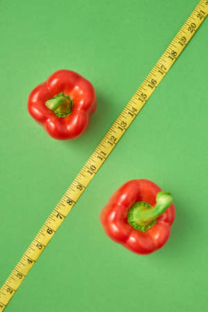 Creative composition from two red paprika pepper and diagonal yellow measuring tape as the symbol of percent on a green background, copy space. Top view. Low calorie food for reduction of weight.の写真素材