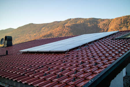Alternative energy solar panels on a tiled roof on a background of stone mountains and clear blue sky in autumn day, Austria.の写真素材