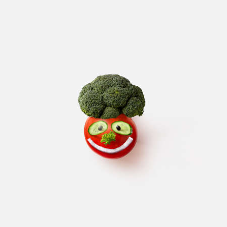 Funny smiling creative face handmade from natural organic vegetables tomato, broccoli and cucumber slices on a white background, copy space. Top view. Vegan concept.の写真素材