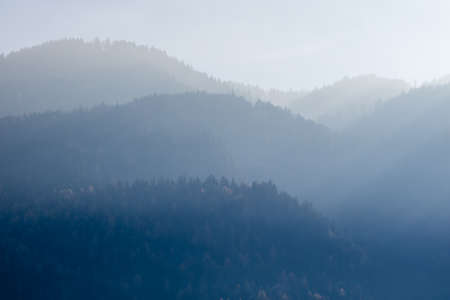 Beautiful tranquil landscape from blurred foggy mountains with trees on a background of sunny clear sky in Kufstein Austria.の写真素材
