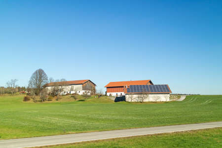 Beautiful landscape with buildings of farming with solar panels on a roof on a green fields and areas on a background of blue clean sky in an autumn time, Austria.の写真素材