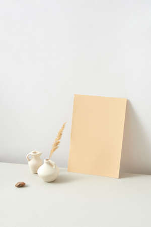 Vertical modern composition from handmade ceramic vases different shapes with natural dry plant twig and vertical paper sheet against light grey background, copy space. Natural eco concept.の写真素材