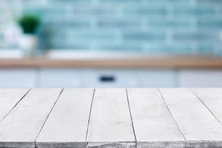 Empty white wooden boards or table top over blurred kitchen interior on background. Template, mockup for display or montage. Close up, copy spaceの写真素材