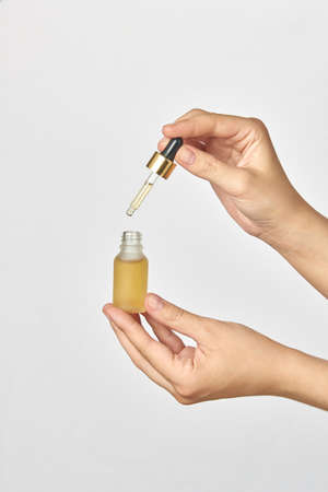 Bottle and pipet of medical cannabis CBD oil in hands against a light grey background.の写真素材