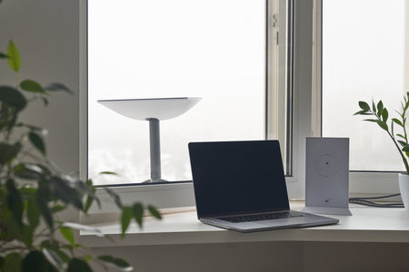 KYIV, UKRAINE - JANUARY 24, 2023: Starlink antenna behind window with wi-fi router and laptop on windowsill in home interior.のeditorial素材