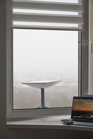 KYIV, UKRAINE - JANUARY 24, 2023: Starlink antenna receiving signal behind window, laptop with Starlink software and smartphone on windowsill.のeditorial素材
