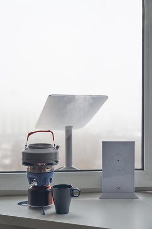 KYIV, UKRAINE - JANUARY 24, 2023: Starlink wi-fi router and antenna by home window with portable burner stove with kettle and cup of tea on windowsill.のeditorial素材