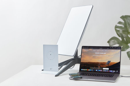 KYIV, UKRAINE - JANUARY 24, 2023: Starlink antenna, wi-fi router and laptop with Starlink software on display on white desk, houseplant in background. Necessities for remote work.のeditorial素材