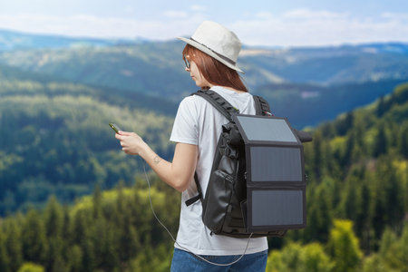 Young woman with mobile phone in hands connected to backpack with portable solar batteryの写真素材