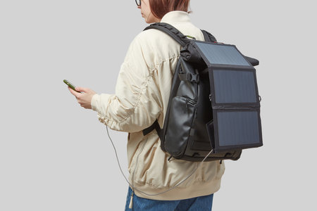 Young woman carrying backpack with flexible solar panel attached to smartphone in her handsの写真素材