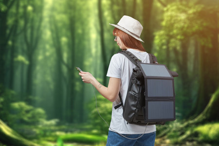 Female hiker with smartphone in hands carrying backpack with charging solar panel onforest backgroundの写真素材