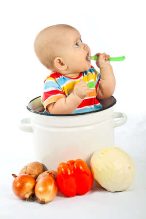 Baby sitting in the big white kitchen saucepan with vegetables.の写真素材