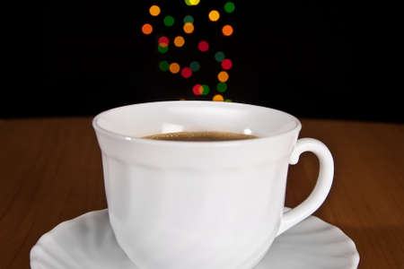 Cup of coffee on wooden table with many-colored sparkles の写真素材