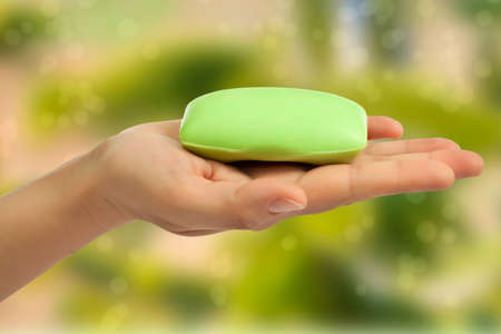 Green soap bar in hand on green abstract background の写真素材