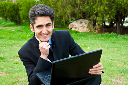 Young man is working on laptop in the park on the bench.の写真素材