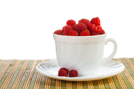ripe wild raspberries in  white cup on straw napkin