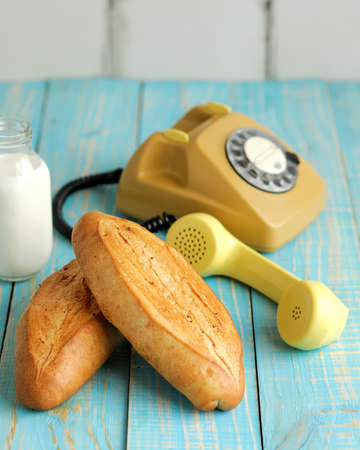 Freshly bakery food and old telephone in retro style. White bread loafs and glass of milk. Light...