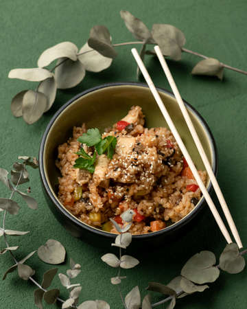 Asian lunch. Bowl of stew with sesame seeds and chinese chopsticks on green background. Top view. Traditional Oriental vegetable dish. Vegetarian or vegan cuisine. Vertical format, 4x5.の写真素材