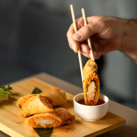 Man Eating Rolls with Sauce Using Chinese Chopsticks. Delicious oriental dish, close up. Eastern Cuisine. Food concept. Square format or 1x1 for posting on social media. Soft focus.の写真素材