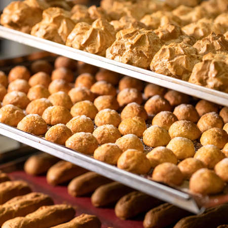 Profiteroles and eclairs, puff pastry baked goods on shelves of bakery or cafe. Fresh baked dough....