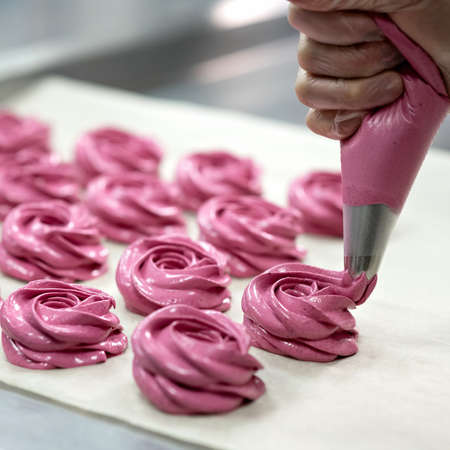 Marshmallow cooking process. Chef squeezes pink rose shaped Marshmallows out of pastry bag on parchment paper, Close up. Homemade baking business. Sweets for loved one or holiday event. Soft focus.の写真素材