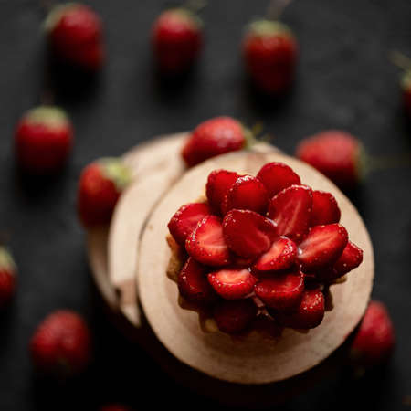 Mini Cake with fresh berries. Chopped strawberries at top of Berry tart, dough baskets. Cake tartlet dessert on black background. Summer seasonal sweets, healthy goodies. High angle view. Soft focus.の写真素材