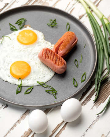 Fried eggs, sausages and green onions in frying pan. Classic American or English breakfast on rustic table.の写真素材