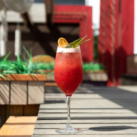 Alcoholic drink. Glass of red tropical cocktail against of sun terrace on blurred background. Vacation concept.の写真素材