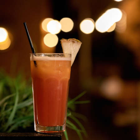 Glass with orange cocktail beverage with lemon slice and straw against of blurred backlit background. Alcoholic or non-alcoholic drink. Close up shot. Copy space at right side.の写真素材