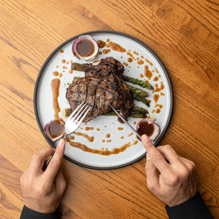 Male hands with knife, fork and Food plate with Juicy grilled steak. Man having lunch in restaurant....