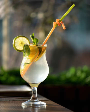 Glass of refreshing drink with straws. Citrus tropical cocktail or lemonade drink with mint leaves on backlit blurred background. Healthy fresh juice or soft drink. Bright colors of nature.の写真素材