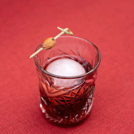 Shot glass of strong alcoholic drink with ice on red fabric tablecloth. Close up shot.