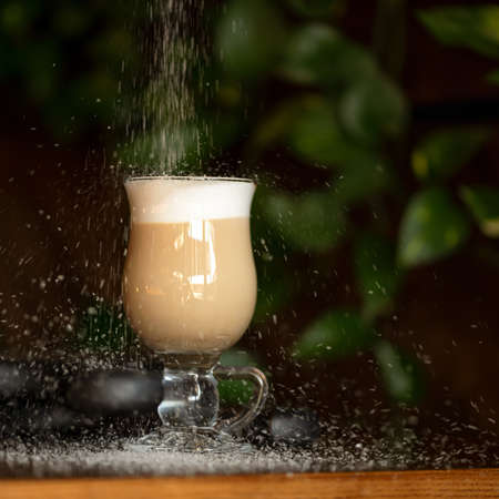 Sugar pouring into glass cup of coffee with milk on dark background. Soft focus. Copy space to right side.の写真素材