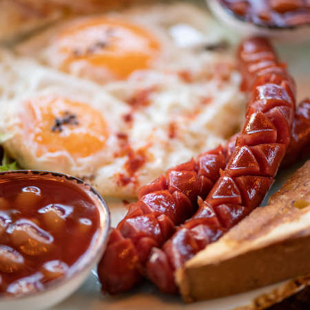 Close up of traditional American breakfast. Selective focus on appetizing sausage. Fried eggs and...