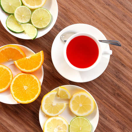 Vitamin Red tea from frozen berries. Flat lay. Cup of drink and saucers with citrus fruits on wooden table. Tea time. Close up shot. Top view.の写真素材