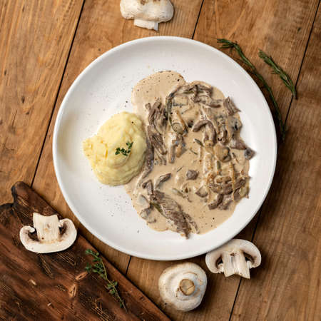Flat lay food. Potatoes and stewed mushrooms with sour cream. Vegetarian lunch or dinner. Dish with mashed potatoes and champignon julienne on wooden background. Top view.の写真素材