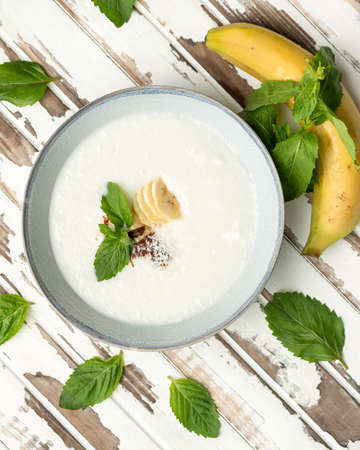 Dairy product with banana and mint leaves on white wooden rustic background. Flat lay food. Nutritious breakfast, wholesome healthy food. High angle view.の写真素材