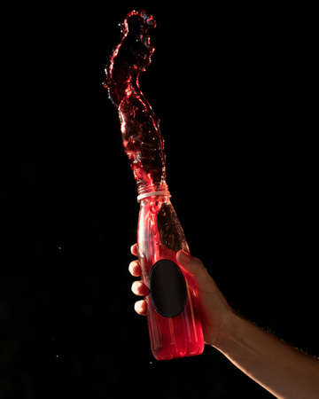 Red Splashing of bottle drink. Refreshing vitamin beverage splash from plastic container on black...